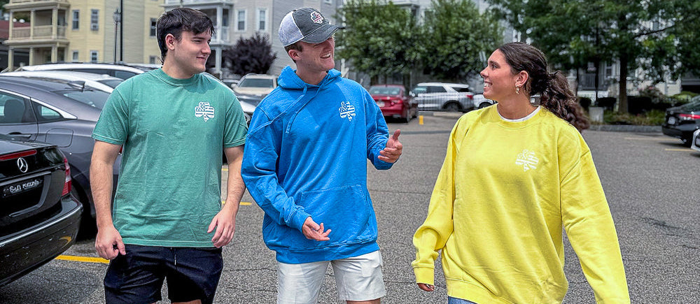 Three people walking together on a street with buildings and cars in the background